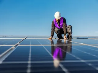 Worker in purple vest and hard hat touching solar panels