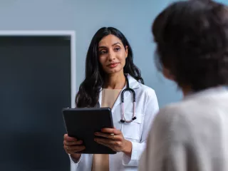 A female doctor in white coat speaks to a patient in a hospital room
